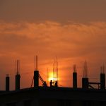 Silhouette of workers on a construction site against a vibrant sunset sky.